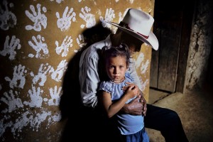 00216_15, HONDURAS-10001, La Fortuna, Honduras, 2004. A man and child against a handprinted wall. Magnum Photos, NYC44610, MCS2004002 K001 "Against a wall surrealistically covered with stencils of hands, a cowboy's big hands hold a little girl. The man, who is the girl's grandfather, is lost in thought, his face hidden in the shadow of his hat. The girl looks out toward the photographer, and through him to his audience, seeking a connection, it appears, though the man clasps her in a firm grip. The picture can stand for the process of bridging cultures - the young, eagerly looking out; the older generation holding fast." - Phaidon 55. Steve Mccurry_Book final print_MACRO final print_Birmingham final print_milan Coffee_Book retouched_Sonny Fabbri 10/15/2014